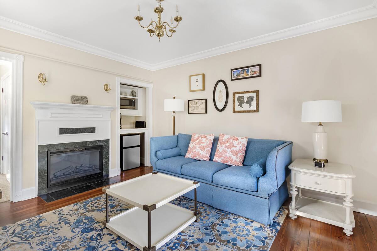A living room with a fireplace, a blue sofa, a white side table, and a patterned rug.