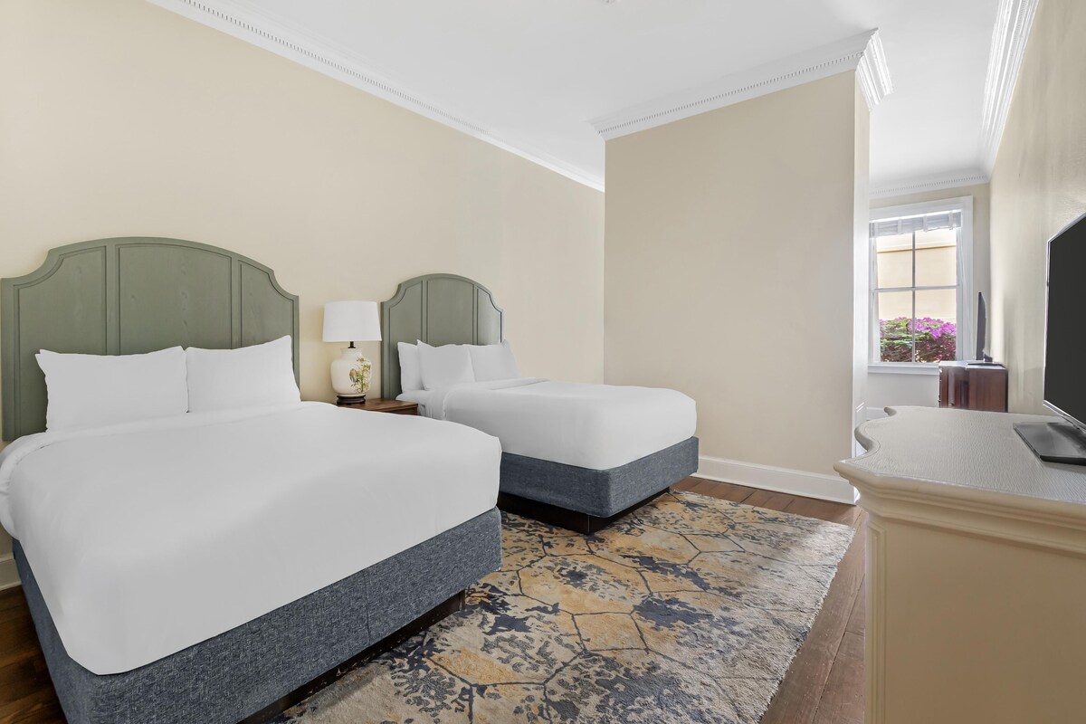 A hotel room with two beds, a TV, a desk, and a window with a view.
