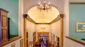 A grand hallway with a high ceiling, a chandelier, and framed pictures on the walls. - Hassayampa Inn (Prescott)