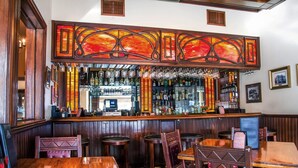 A bar area with wooden furniture, a bar counter, and a variety of bottles and glasses. - Hassayampa Inn (Prescott)