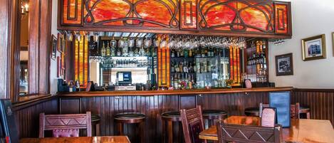 Uma área de bar com móveis de madeira, balcão e diversos copos e garrafas.