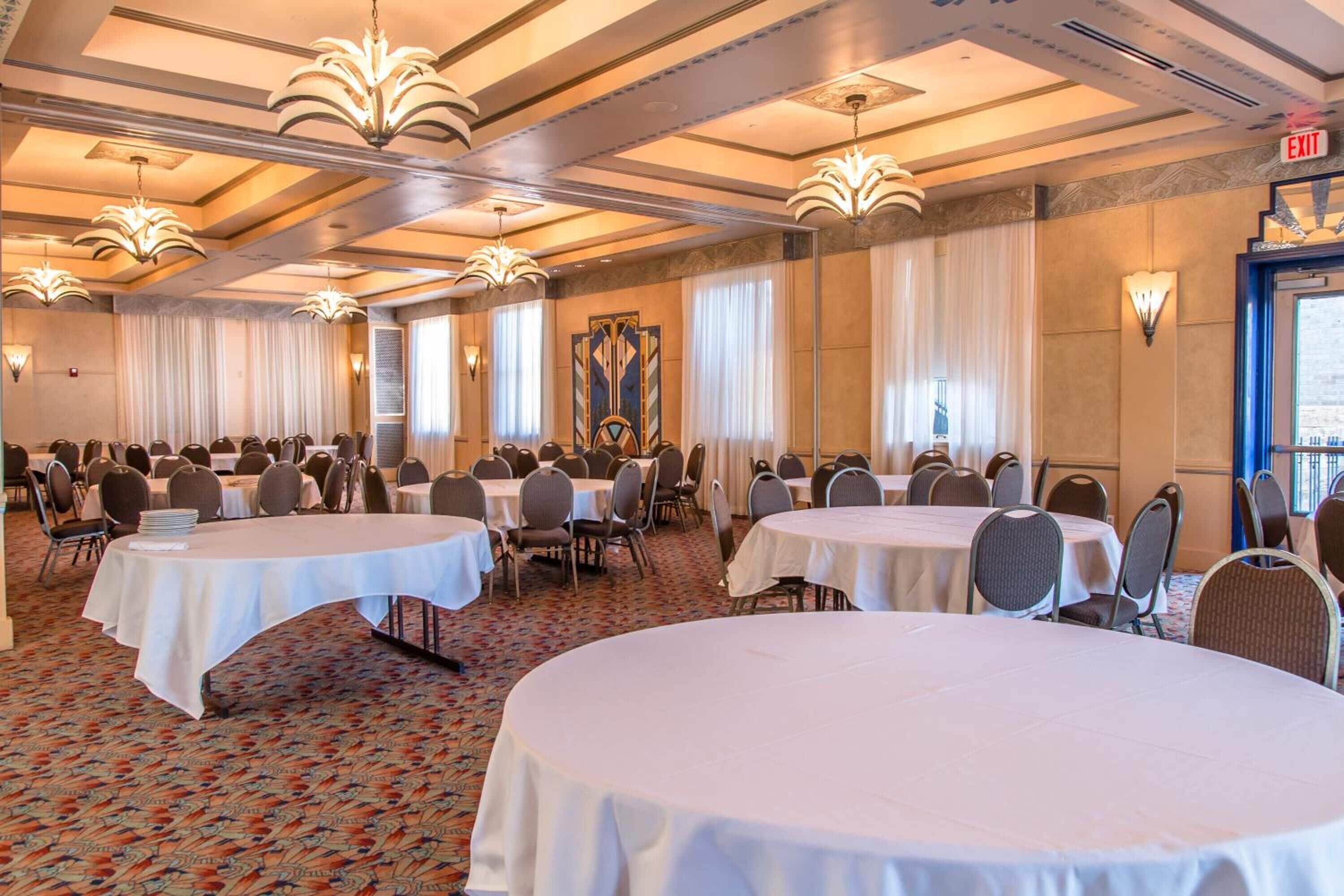 A conference room with multiple tables and chairs, a patterned carpet, and a chandelier.