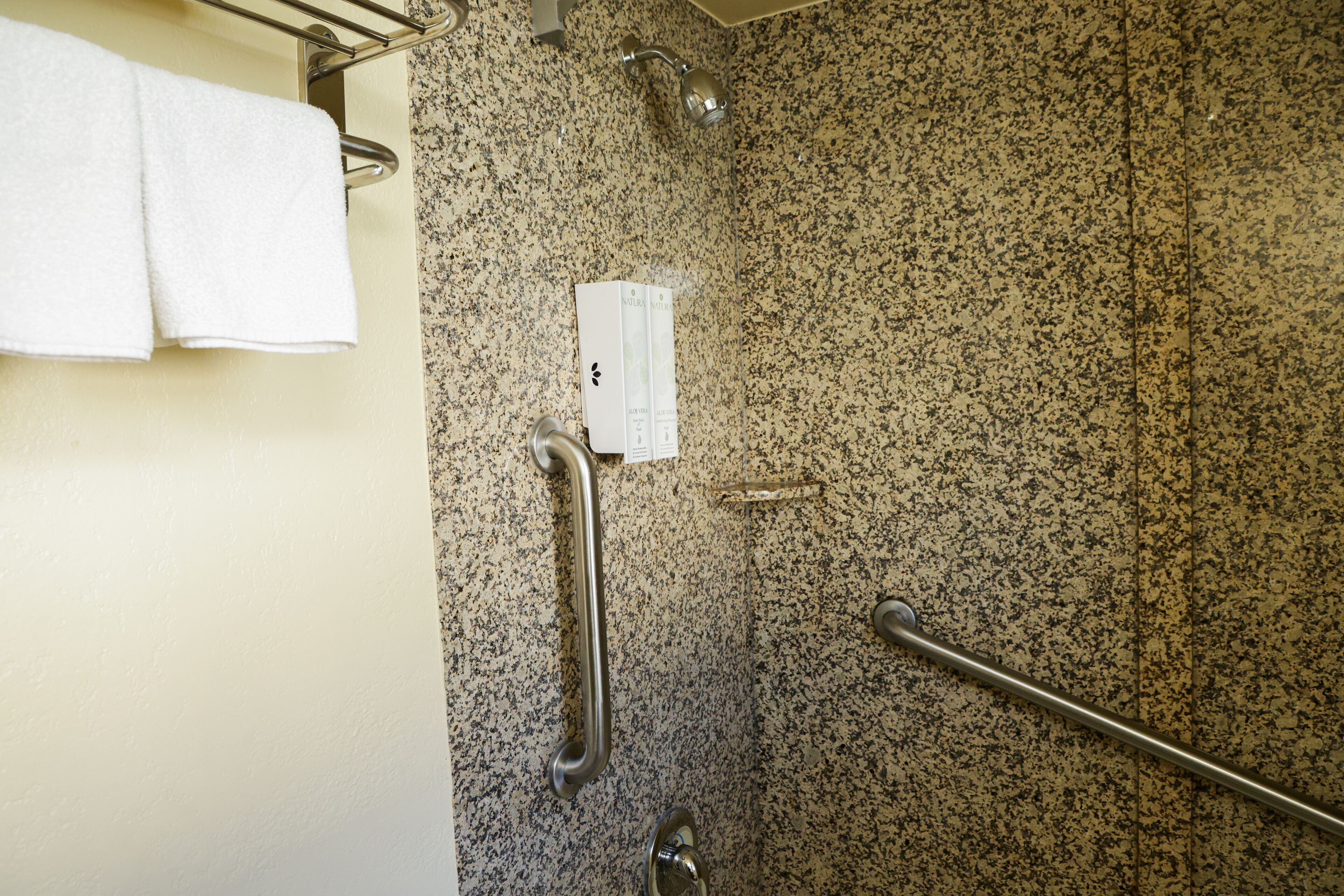 A bathroom with a granite wall, a towel rack, a handrail, and a showerhead.