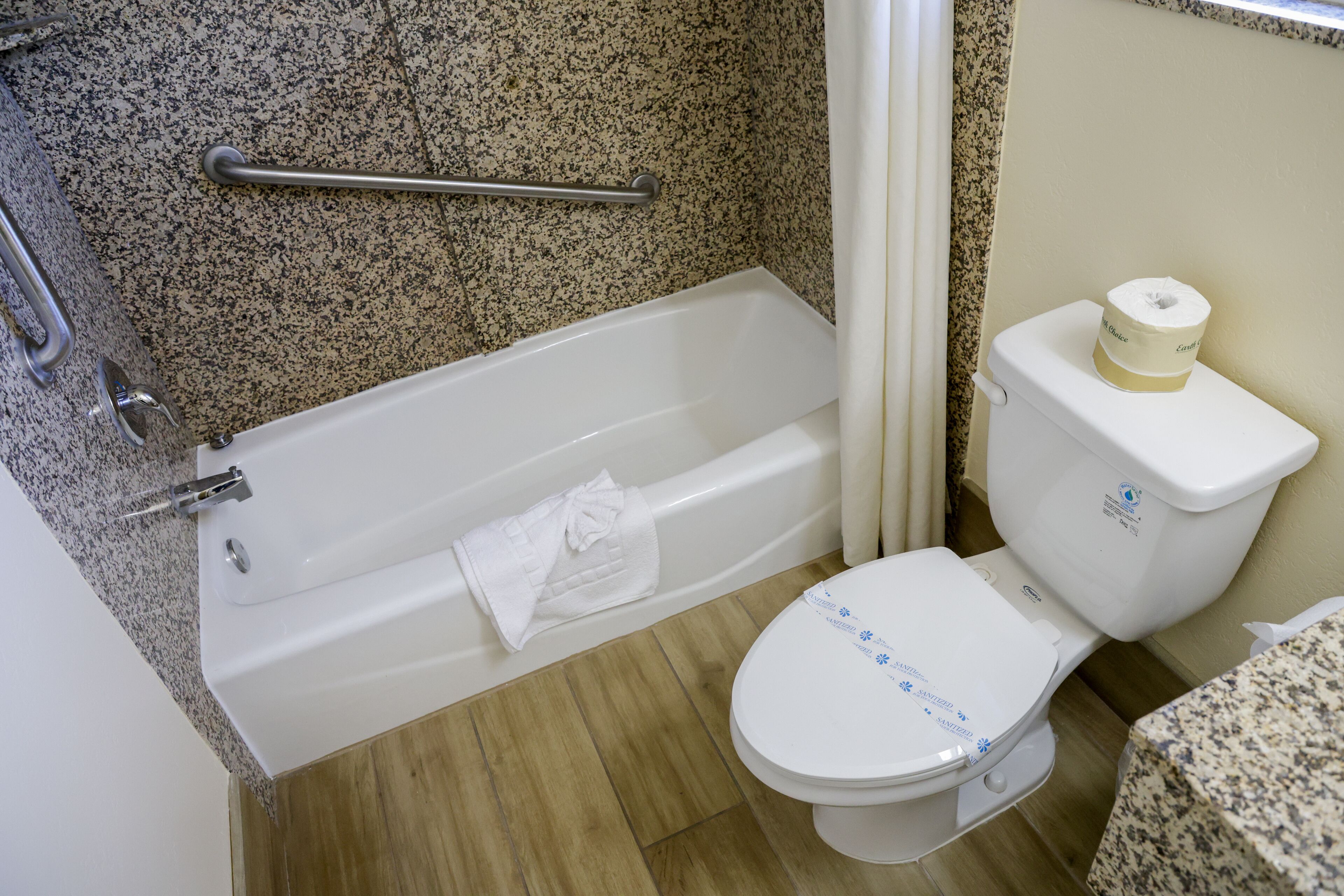 A bathroom with a bathtub, a toilet, and a granite countertop.