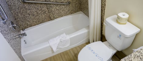 A bathroom with a bathtub, a toilet, and a granite countertop.