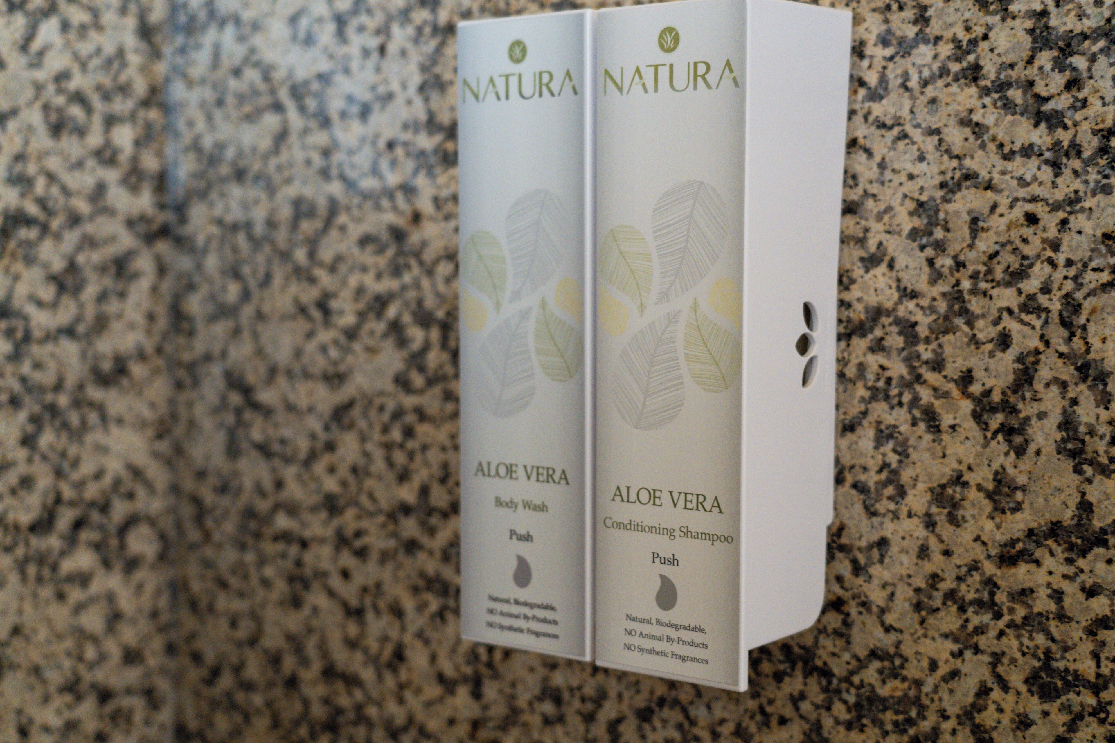 Two Natura Aloe Vera body wash and conditioner boxes on a granite countertop.