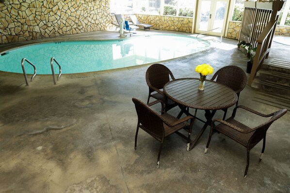 Un espace piscine agrémenté d’un mur en pierre, d’une piscine, de chaises longues et d’une table avec des chaises.