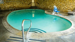 An indoor swimming pool with a stone wall, a pool ladder, and two lounge chairs. - Silver Surf Motel (San Simeon)