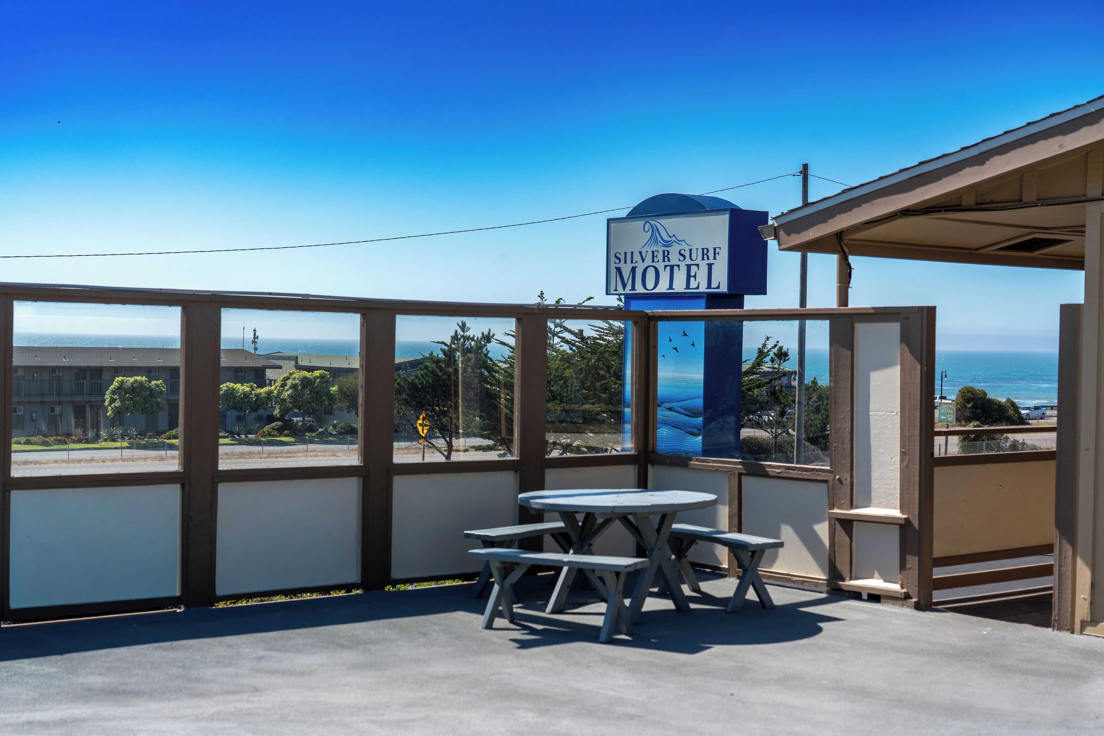 A motel with a view of the ocean, outdoor seating, and a sign for the Silver Surf Motel.
