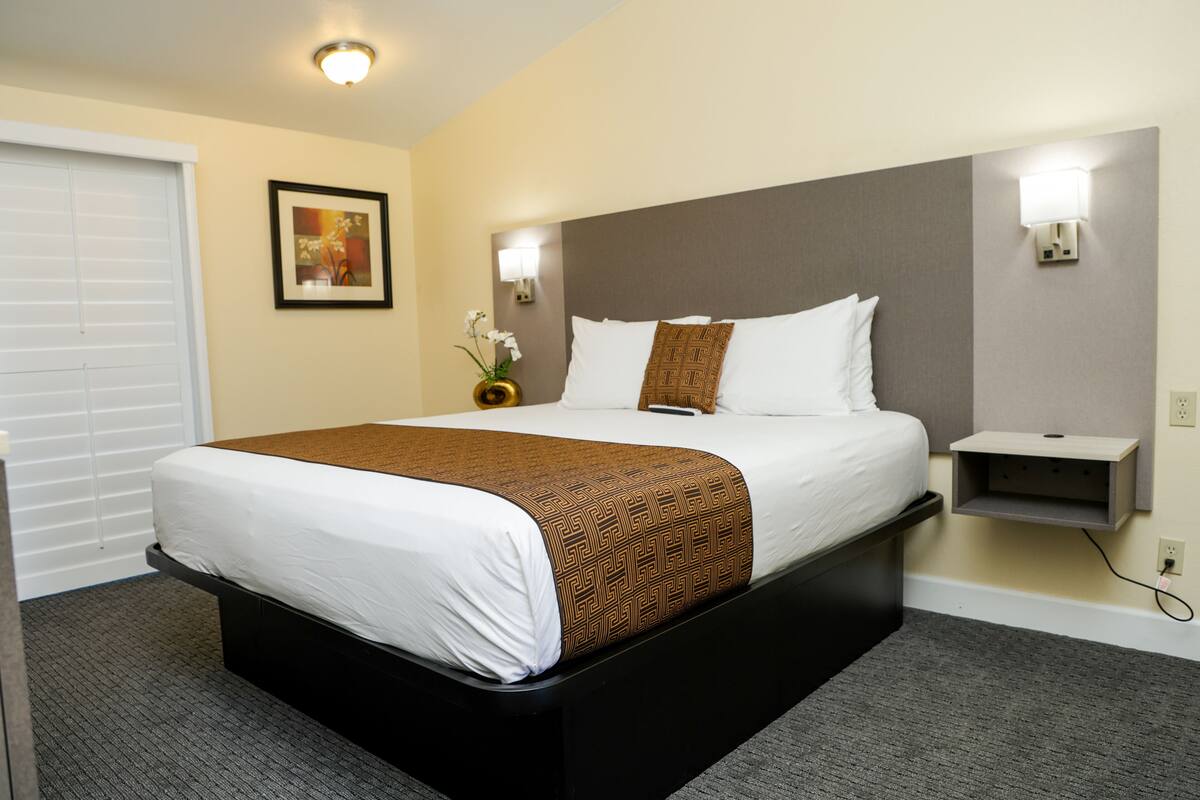 A hotel room with a large bed, a nightstand, a wall-mounted shelf, and a picture on the wall.