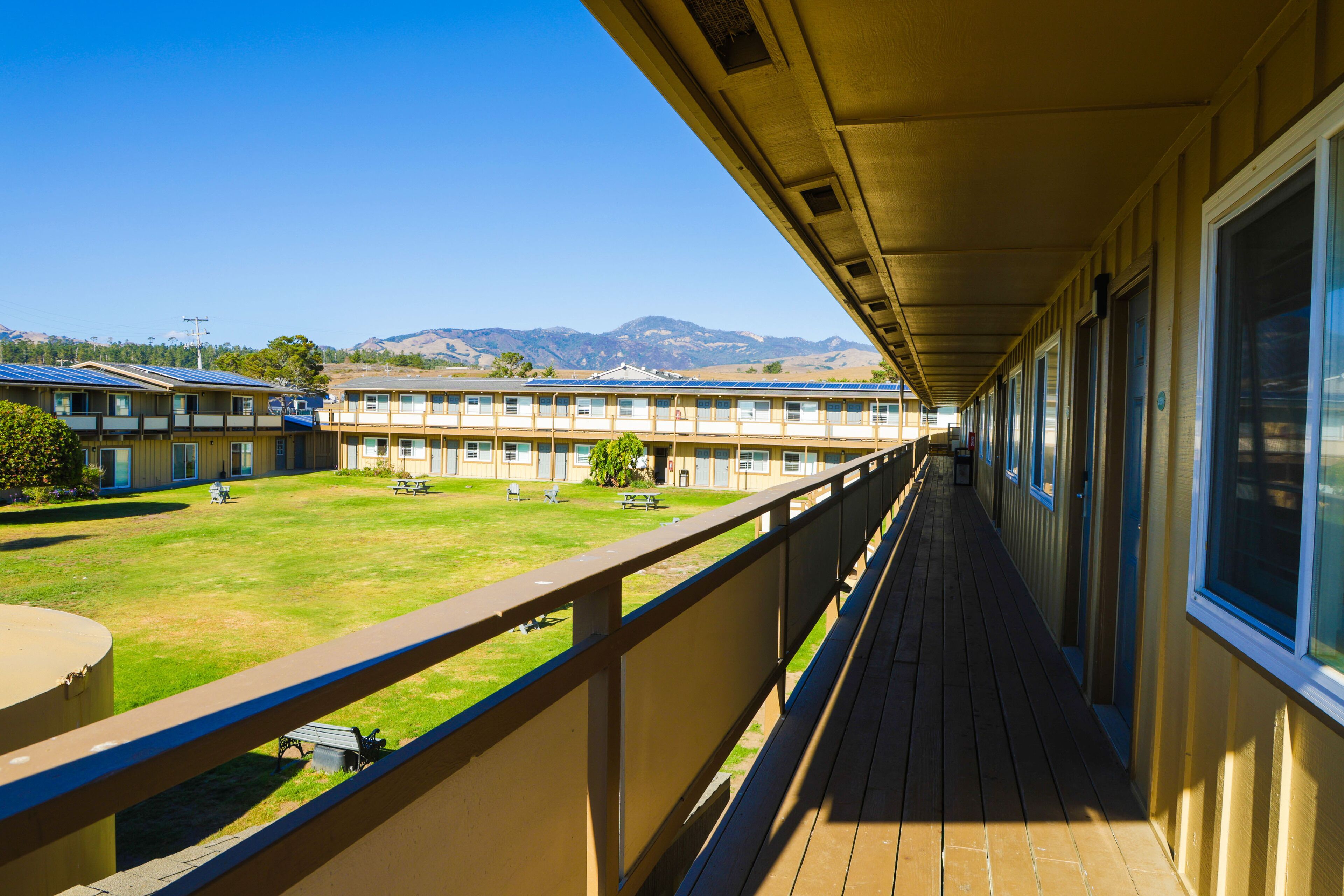 A long corridor with a balcony overlooking a grassy area and a row of buildings.