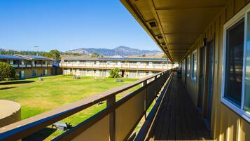 A long corridor with a balcony overlooking a grassy area and a row of buildings.