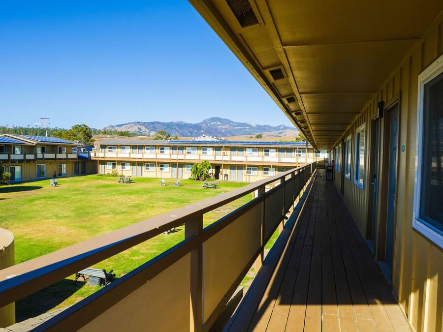 A long corridor with a balcony overlooking a grassy area and a row of buildings.