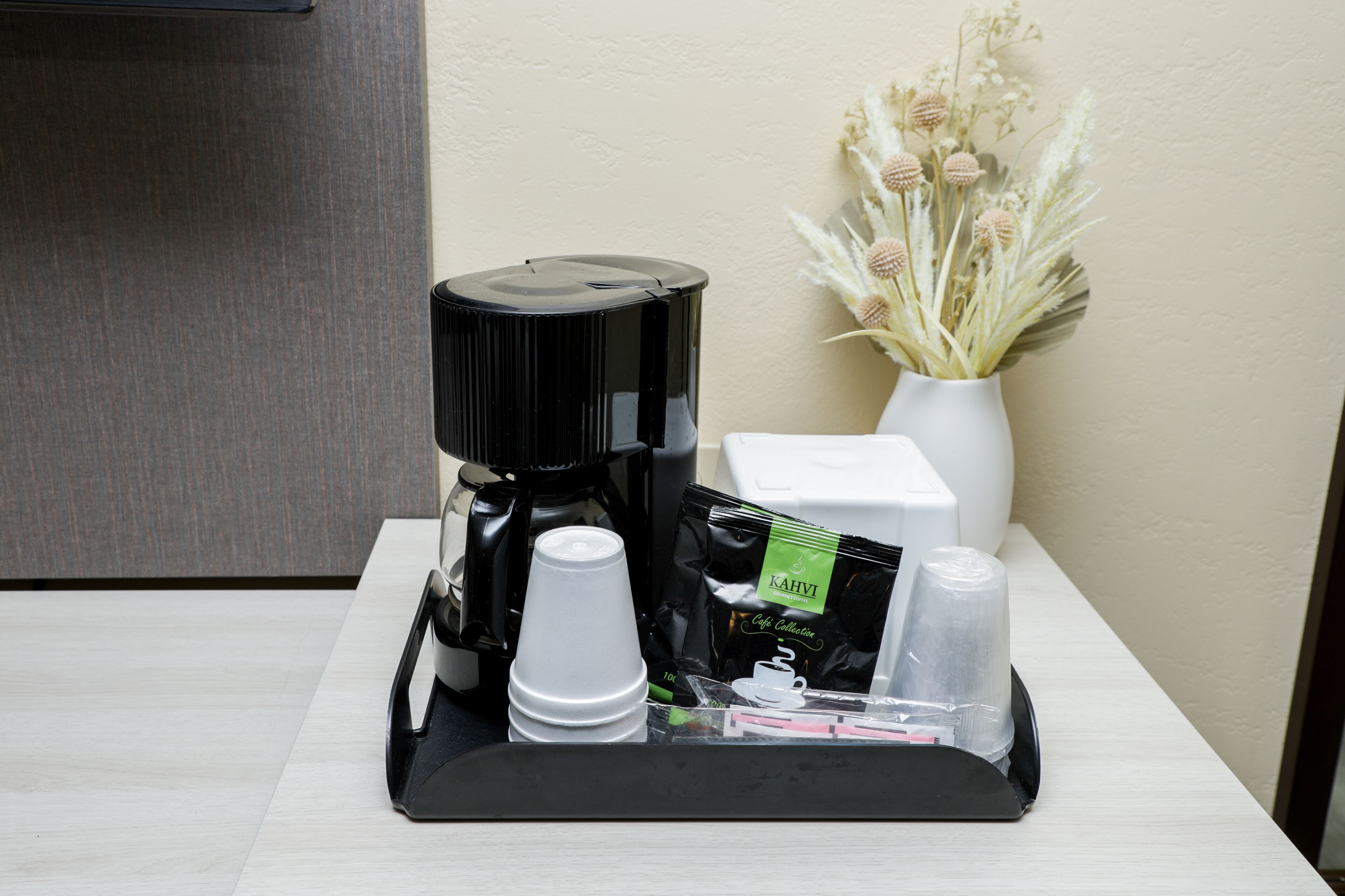 Un coin café comprenant une machine à café, des tasses, un plateau, un paquet de café et un vase avec des fleurs séchées.