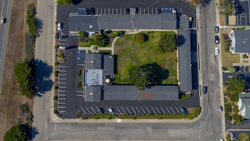 Vista aérea de un estacionamiento con múltiples filas de coches aparcados, una zona verde central y edificios circundantes.
