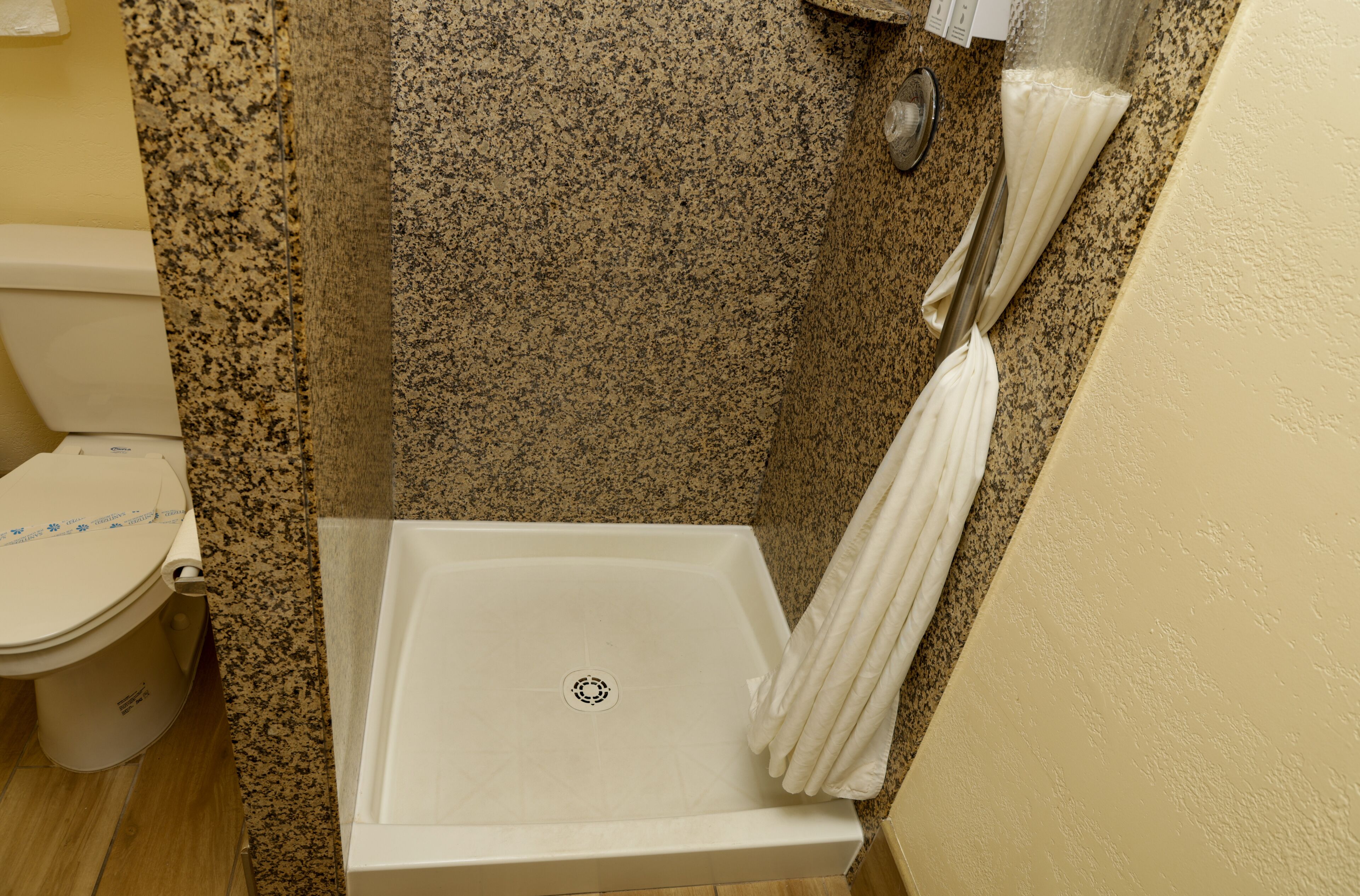 A shower area with a white tub, a granite shower wall, and a toilet.