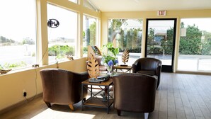 A spacious lobby with leather chairs, a wooden coffee table, and large windows offering a view of the parking lot and greenery outside. - Silver Surf Motel (San Simeon)