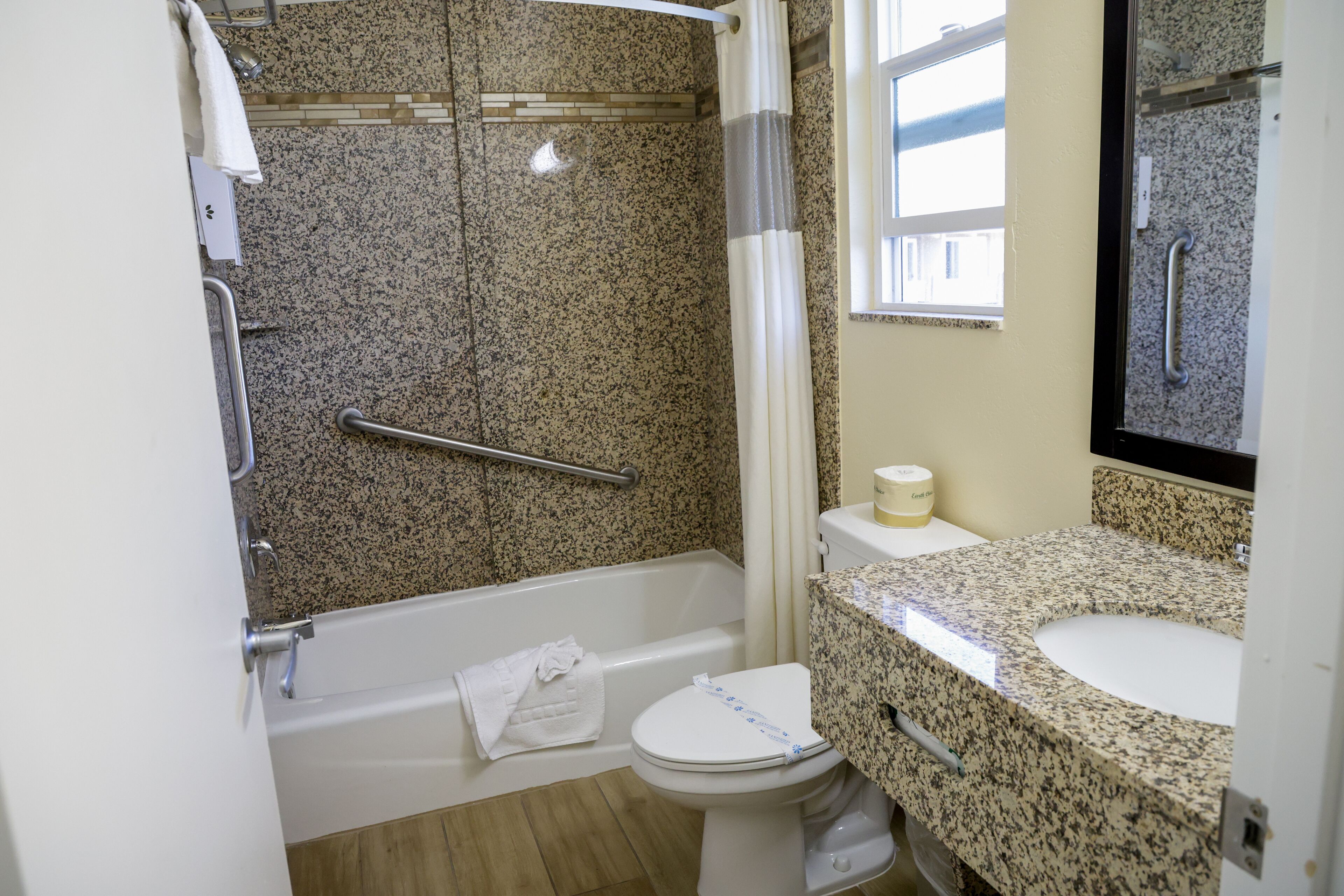 A bathroom with a granite countertop sink, a white toilet, a shower with a grab bar, and a glass shower door.