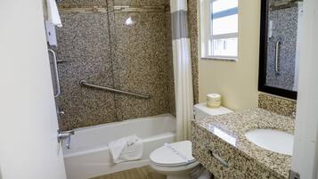 A bathroom with a granite countertop sink, a white toilet, a shower with a grab bar, and a glass shower door.