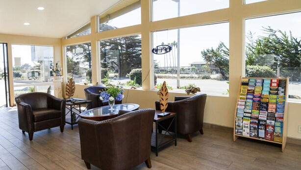 A spacious room with large windows, leather chairs, a glass table, and a travel information stand. - Silver Surf Motel (San Simeon)