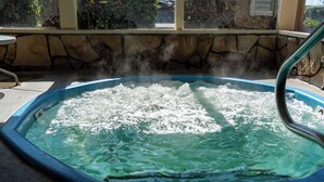 A hot tub with steam rising from the water, surrounded by stone walls and a window. - Silver Surf Motel (San Simeon)