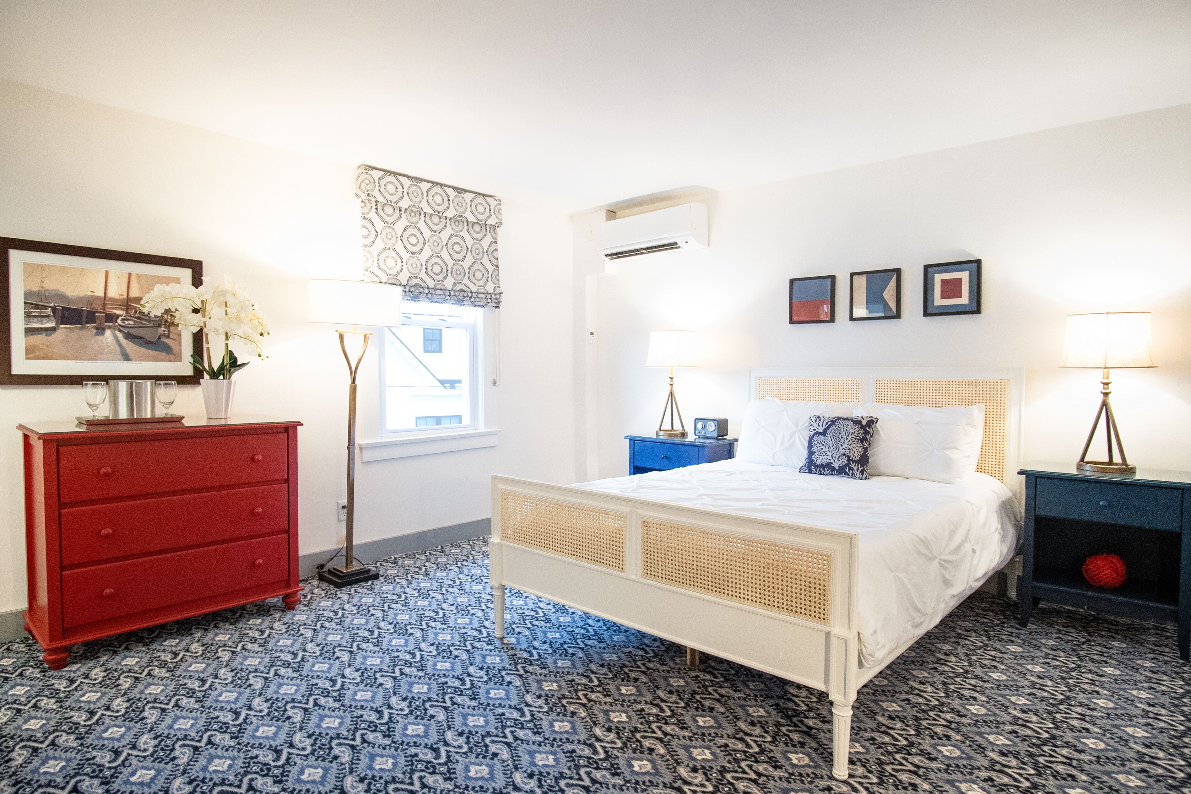 Un dormitorio con cama blanca, cómoda roja y suelo estampado.