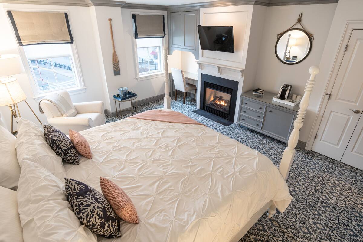 Une chambre d’hôtel avec un grand lit, une cheminée, un téléviseur fixé au-dessus, un bureau avec une chaise et une fenêtre donnant sur un beau paysage.