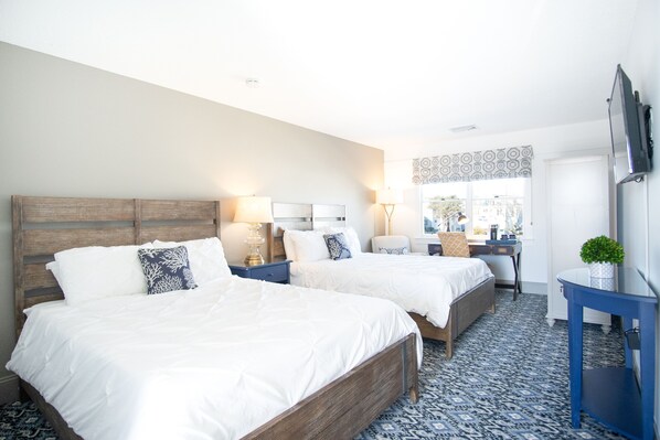 Two single beds with white comforters and decorative pillows, a flat-screen TV, and a potted plant adorn this stylish room.