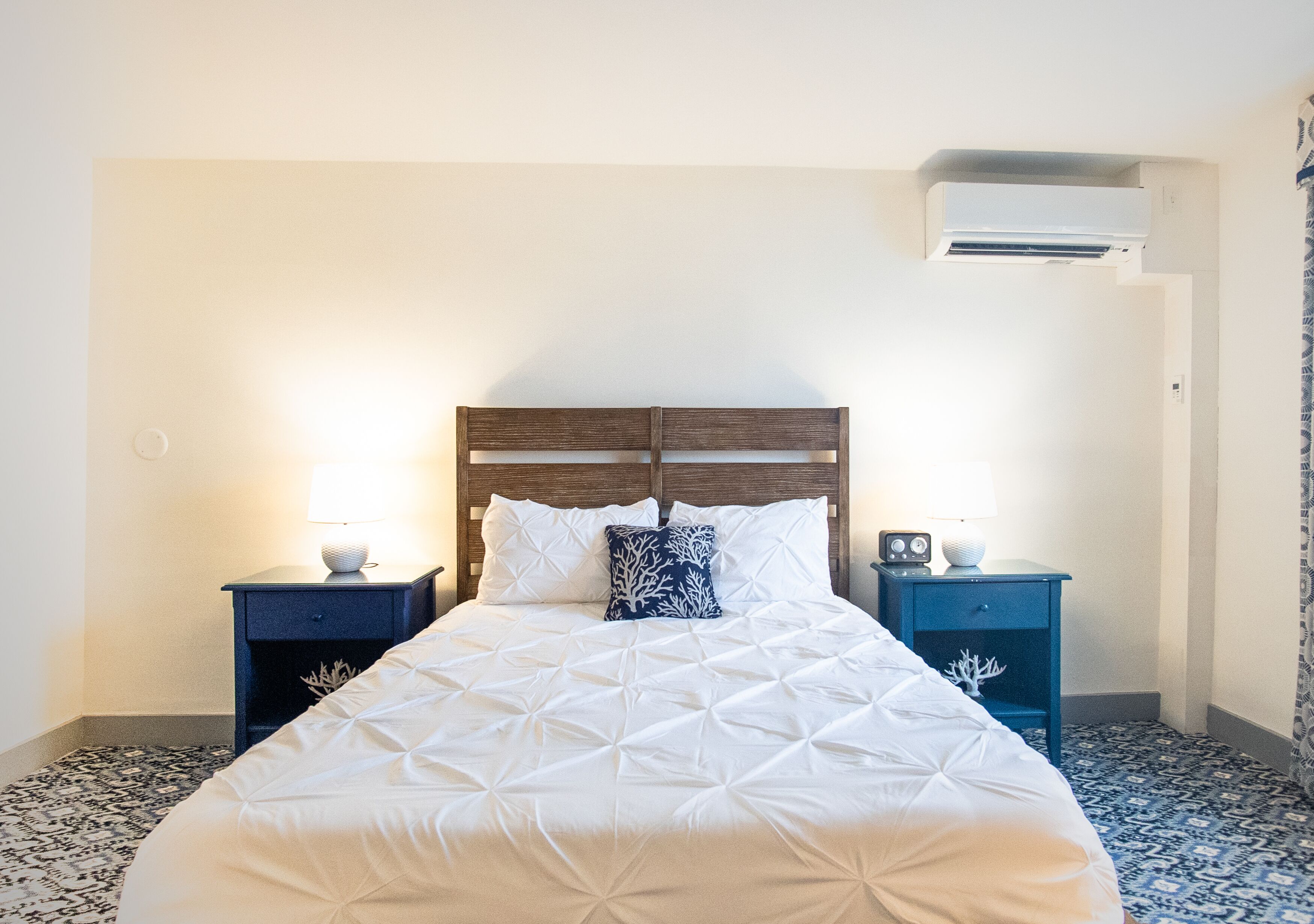 A neatly made bed with a wooden headboard, two bedside tables with lamps, and a patterned floor.