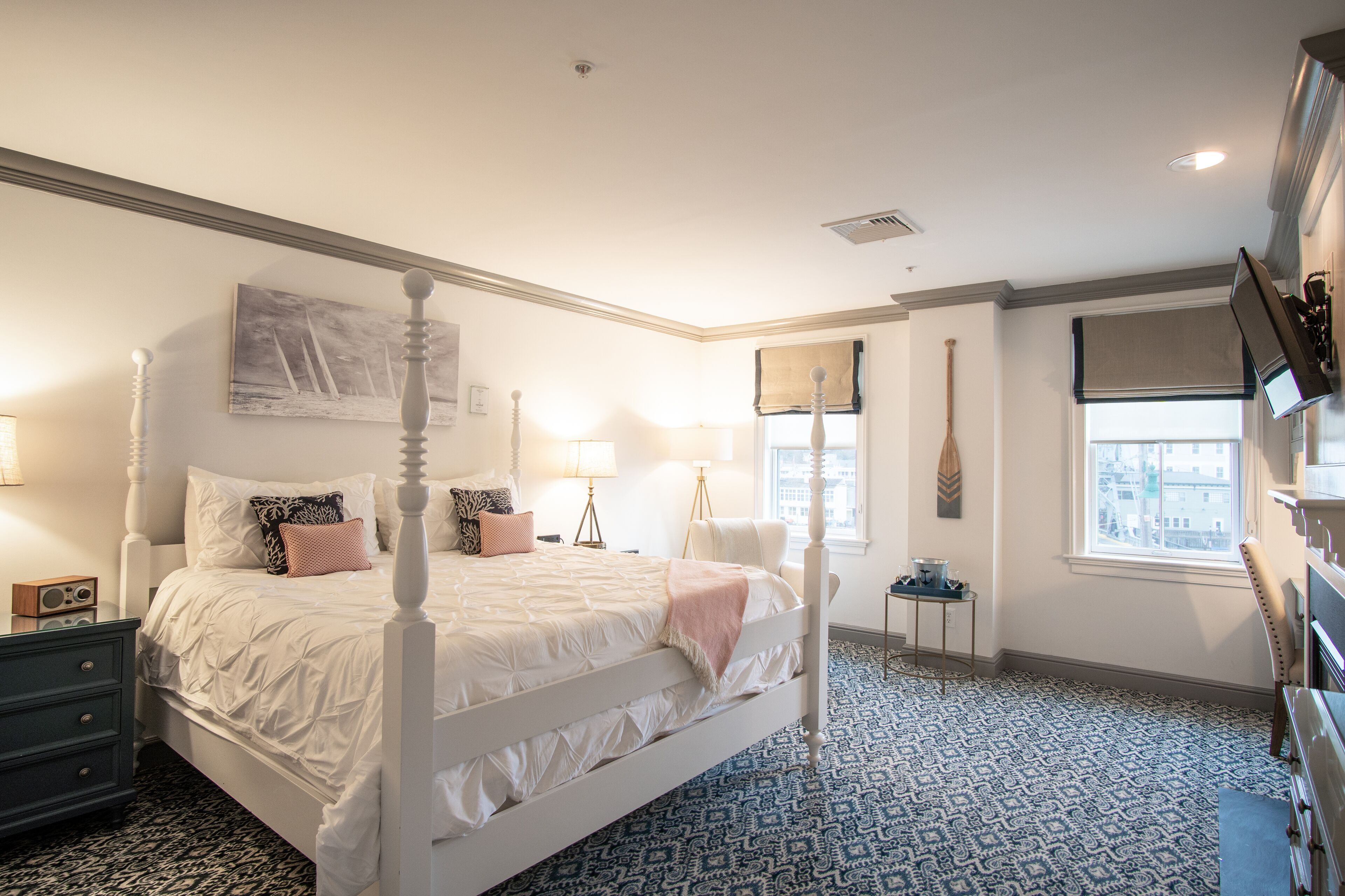 Um quarto com cama de dossel, uma mesinha de cabeceira, uma luminária e uma janela com vista para edifícios.