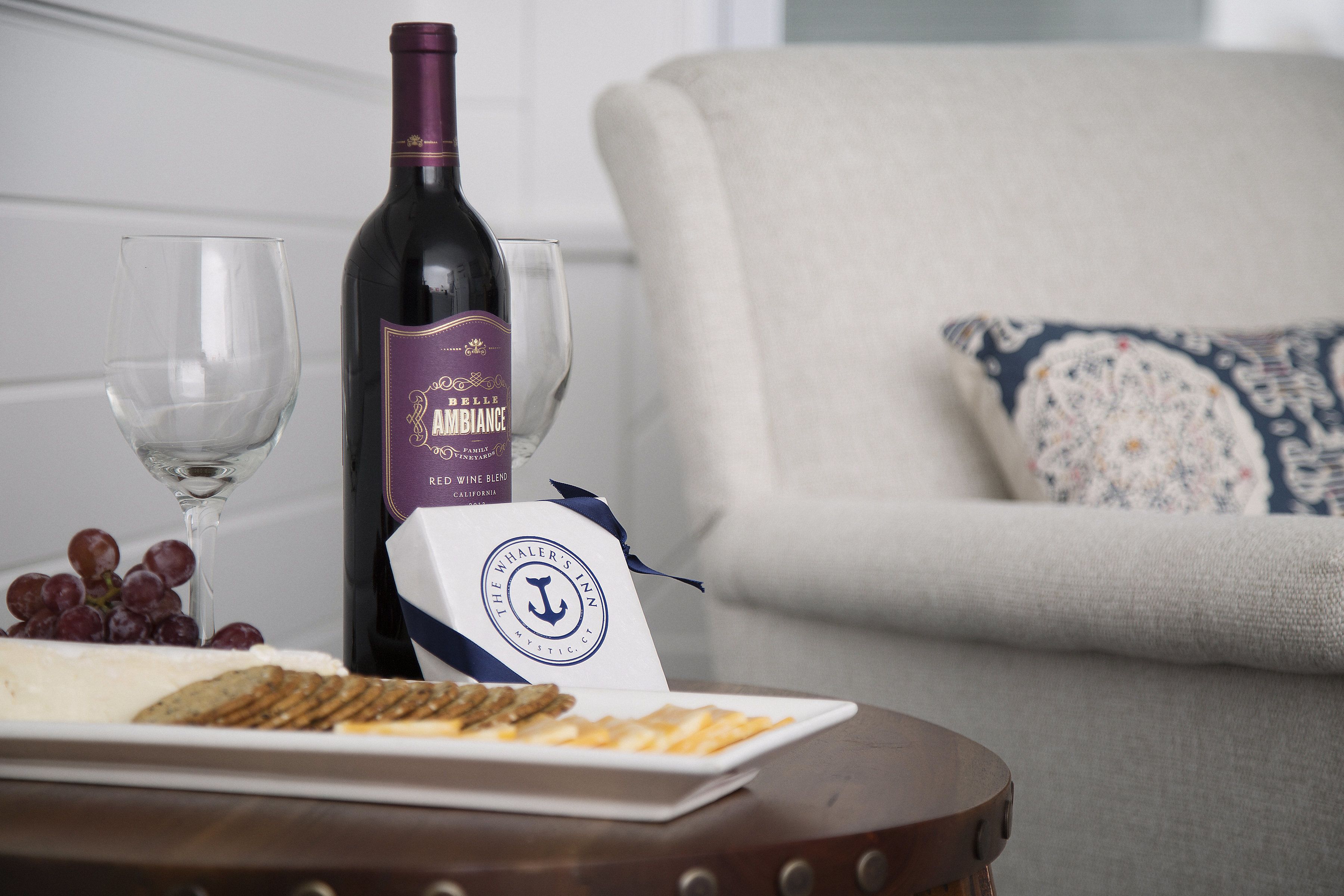 Une bouteille de vin, un verre et une planche à fromage sont posés sur une table, avec un coussin en arrière-plan.