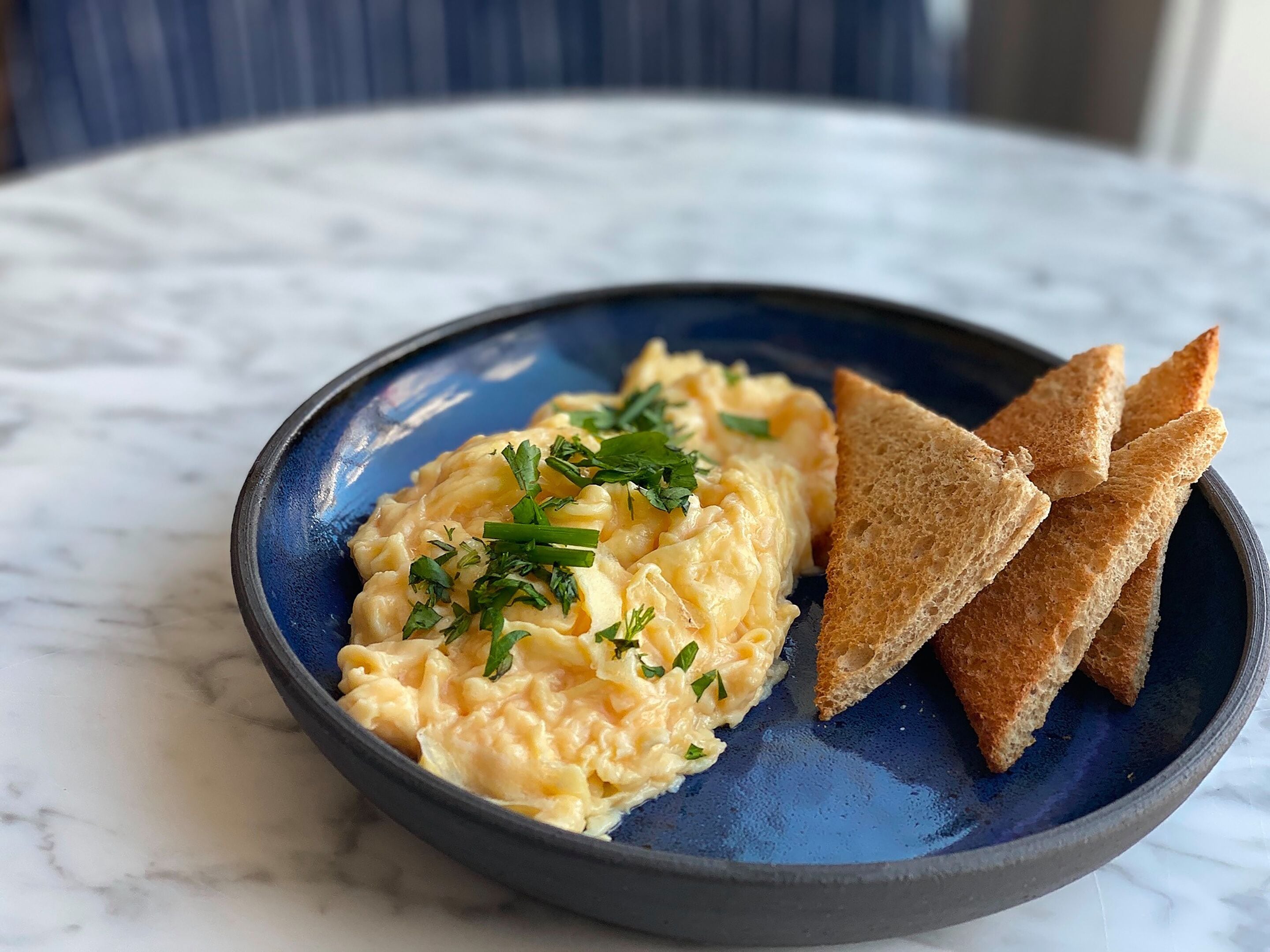 A plate of scrambled eggs with chopped chives, accompanied by toasted bread slices on a blue plate.