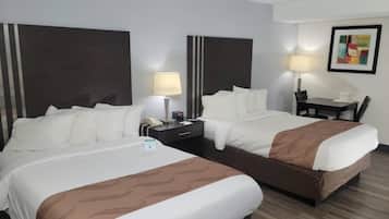 Habitación de hotel con dos camas, un escritorio, una silla, una lámpara y un cuadro en la pared.