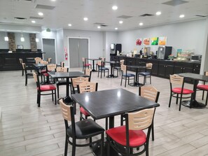 Un restaurante con varias mesas y sillas, una zona de cocina y una barra.