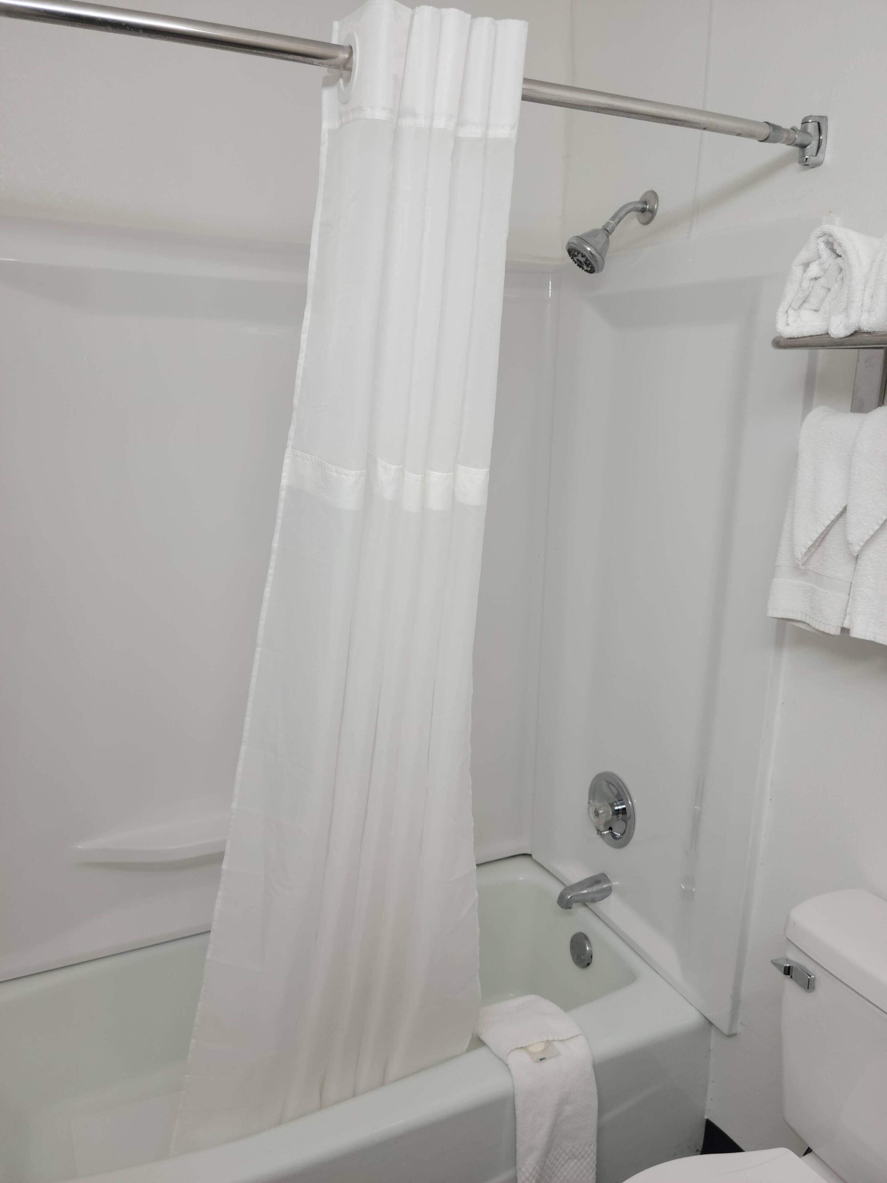 A bathroom with a bathtub, a shower curtain, a towel rack with towels, and a toilet.