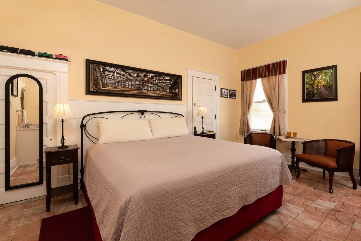 Une chambre d’hôtel avec un grand lit, un bureau, une chaise, un miroir et une fenêtre avec des rideaux.