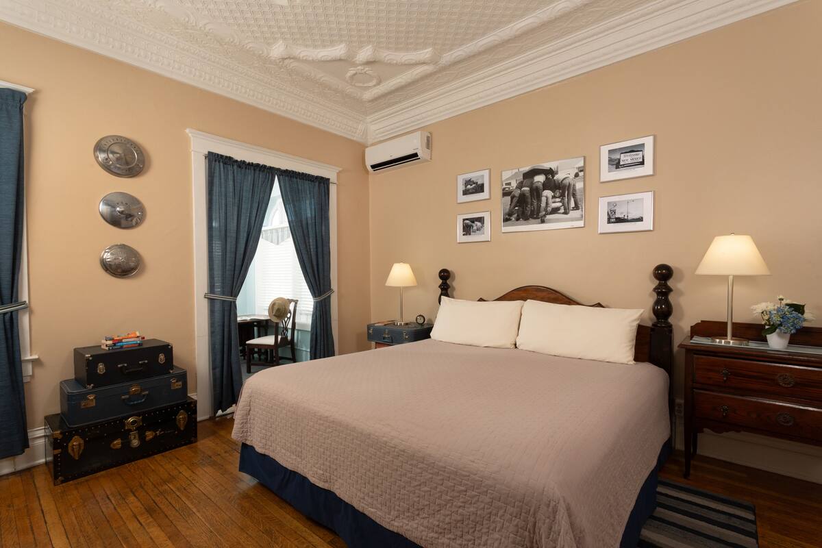 Une chambre bien rangée, avec un grand lit, une commode, une table de chevet et une fenêtre avec des rideaux.