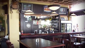 A bar area with a counter, shelves of bottles, and hanging lights. There are tables and chairs for seating. - Arrow Hotel (Broken Bow)