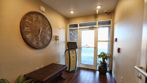 A hallway with a large wall clock, a bench, a vending machine, and a potted plant. - Arrow Hotel (Broken Bow)
