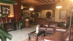 A lobby with a leather sofa, a coffee table, a red and black patterned rug, a wooden reception desk, and a wall-mounted mirror. - Arrow Hotel (Broken Bow)