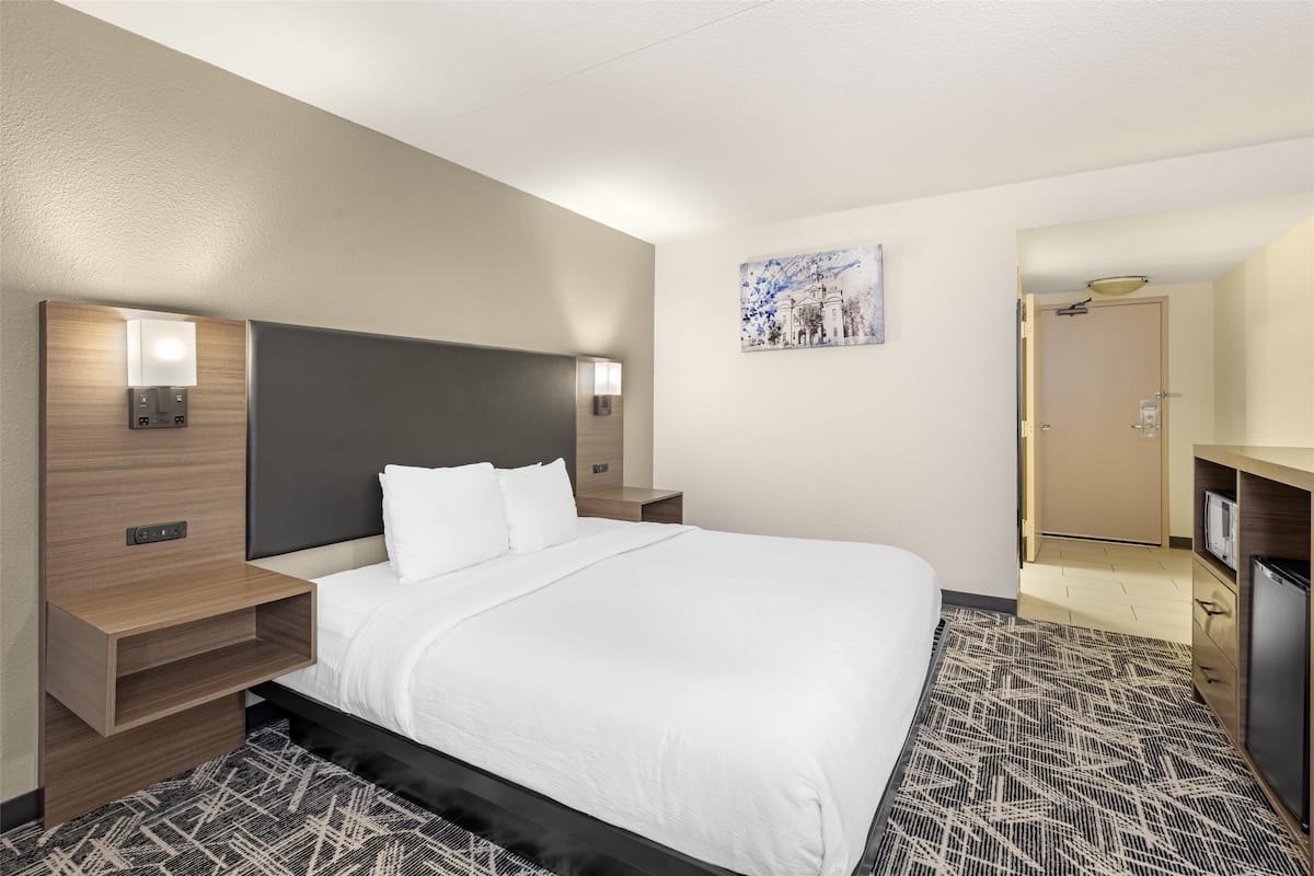 A hotel room with a large bed, bedside tables with lamps, a painting on the wall, and a door leading to a bathroom.