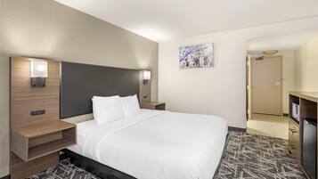 A hotel room with a large bed, bedside tables with lamps, a painting on the wall, and a door leading to a bathroom.