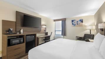 Habitación de hotel con una cama grande, un televisor de pantalla plana, un escritorio con cafetera, un microondas y una zona de estar con una silla y una mesa.