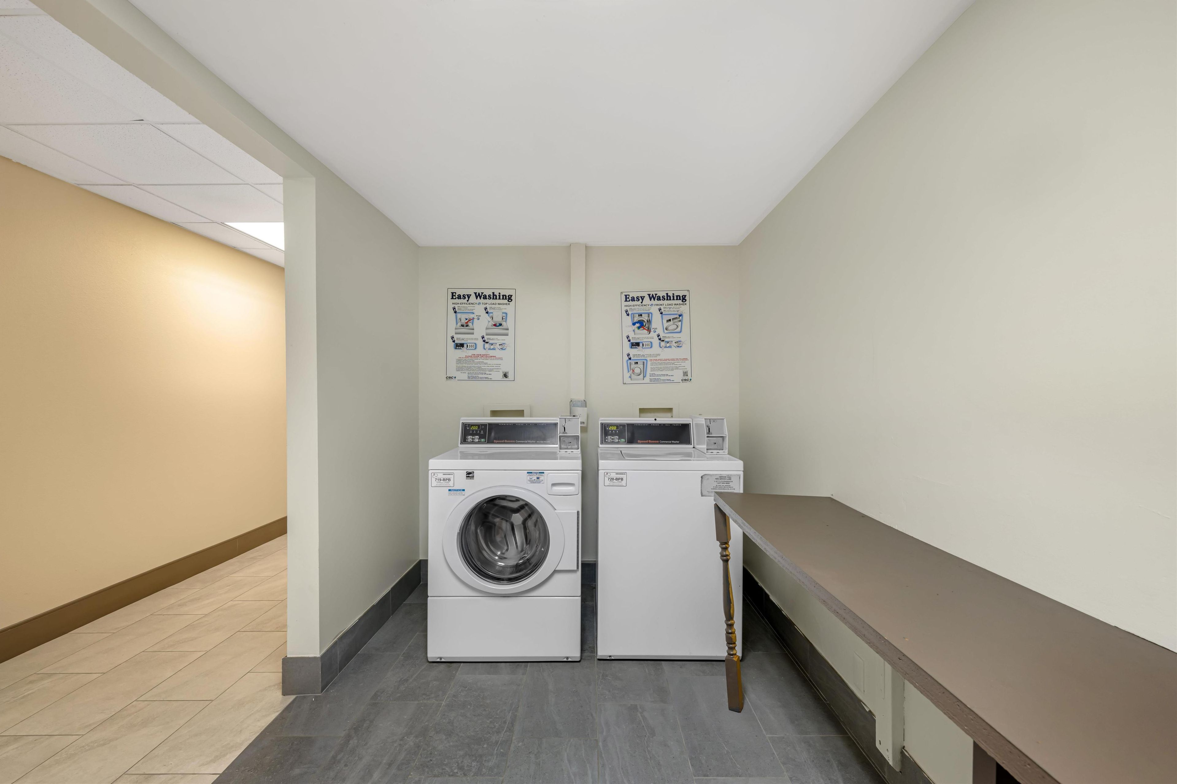 A laundry room with two washing machines, a bench, and two 'Easy Washing' instructional posters on the wall.