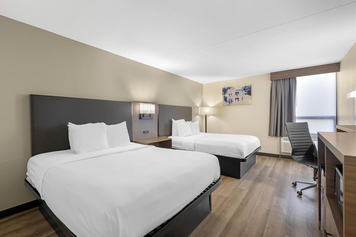 A hotel room with two beds, a desk, a chair, and a large window.