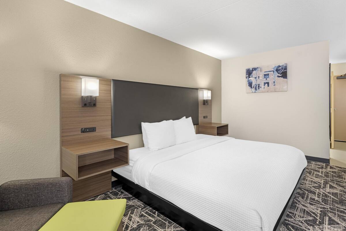 A hotel room with a large bed, wooden headboard, bedside tables with lamps, a small sofa, and a patterned rug.