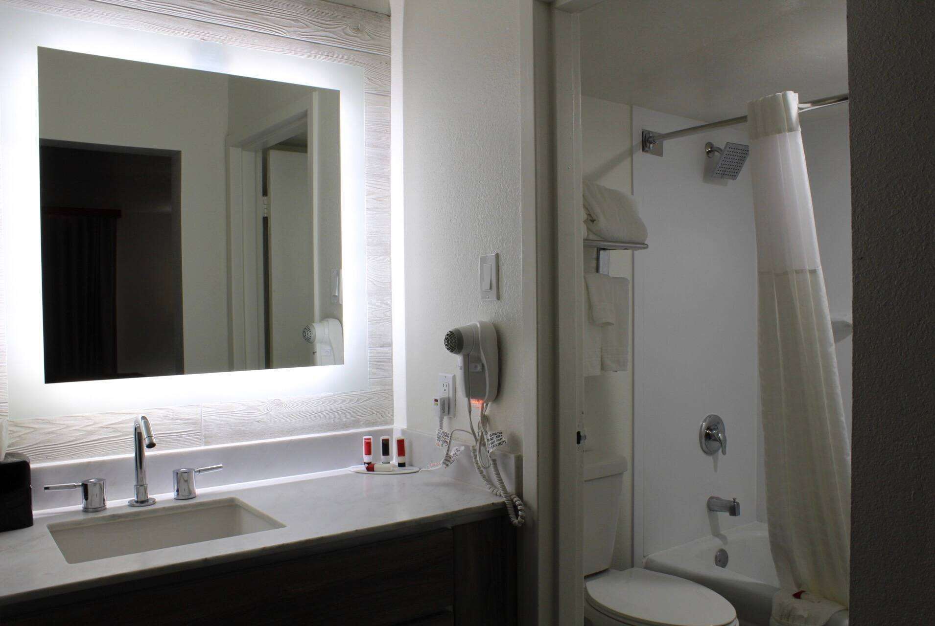 A bathroom with a sink, mirror, hairdryer, and shower.