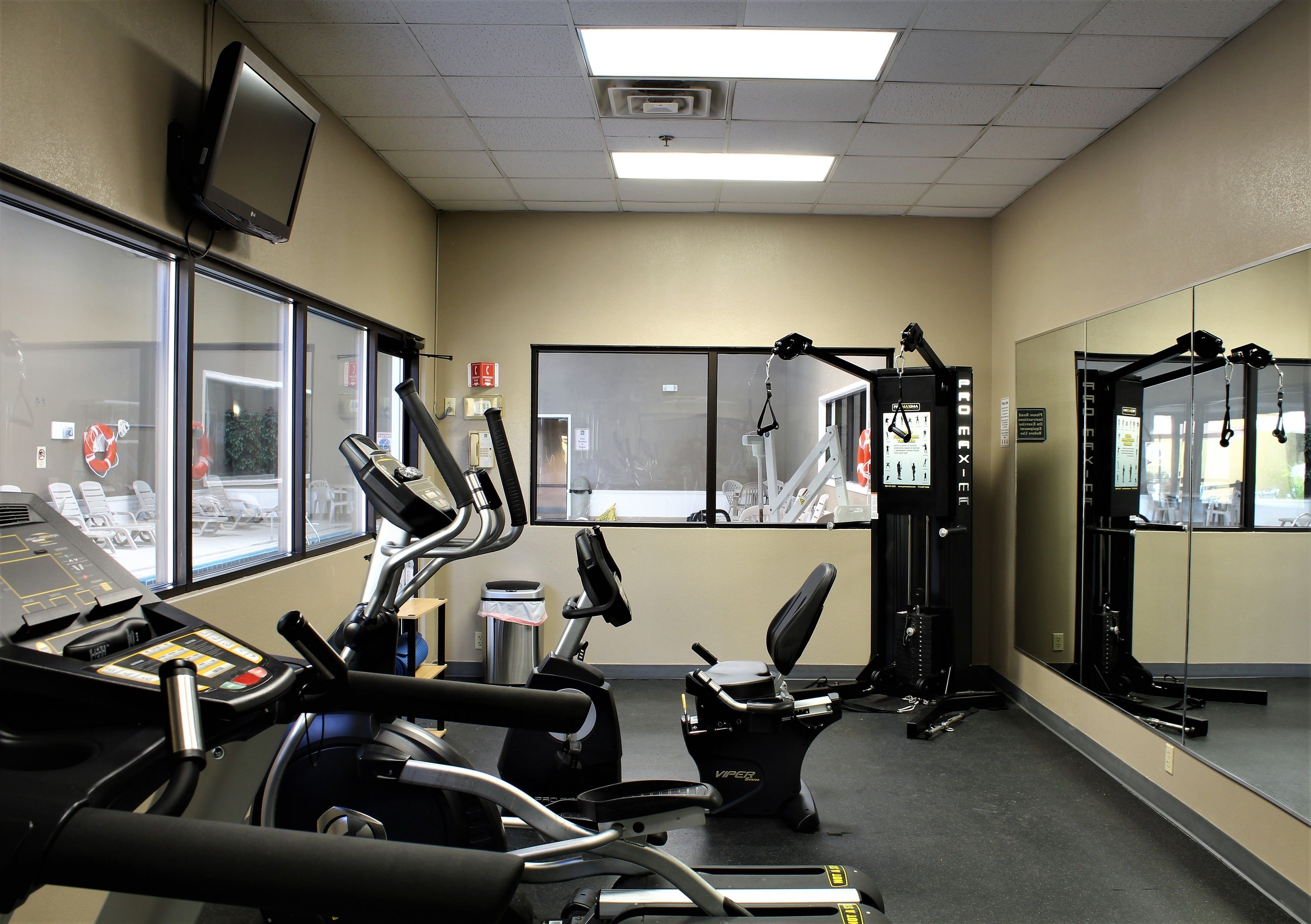 Un gimnasio con equipo de ejercicio, un televisor y ventanas amplias.