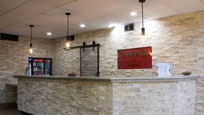 En receptionsdisk med en vägg av sten som bakgrund, ett kylskåp med Coca-Cola och en skylt med texten "RAMADA by WANDA".