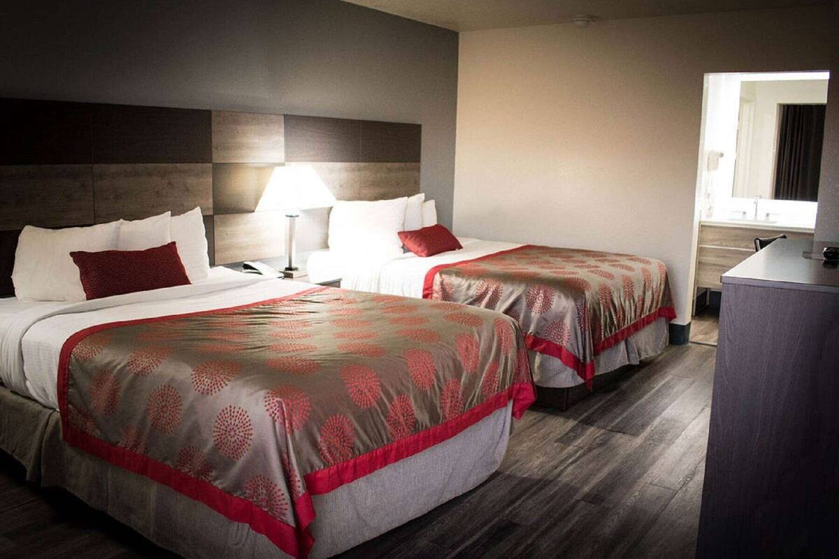 A hotel room with two beds, a desk, and a window.